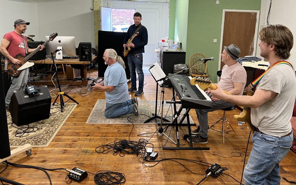 Men in a music studio with various musical instruments including keyboard and guitars