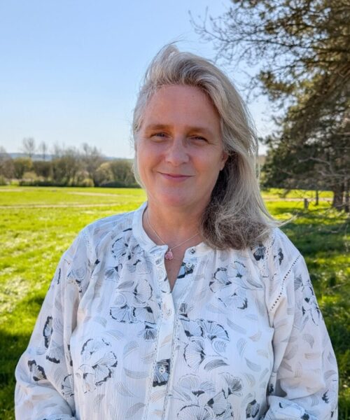 Portrait photo of Hilary stood outside with countryside background